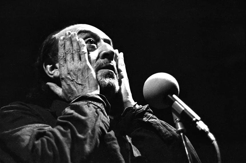 Jean-Roger Caussimon sur scène, mains levées près du micro